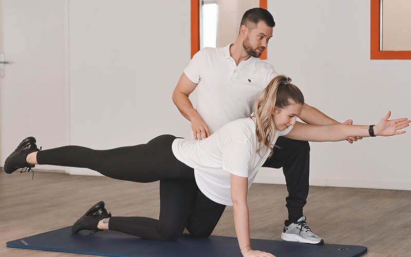 Physiotherapeut unterstützt Patientin bei einer Koordinationsübung im Vierfüßlerstand