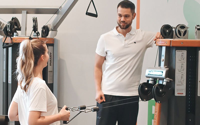 Physiotherapeut betreut Patientin beim Training an Rehageräten