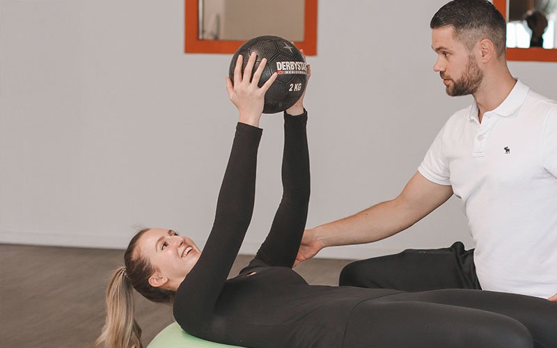 Patientin trainiert mit Medizinball unter Anleitung eines Therapeuten