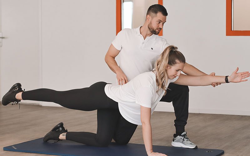 Physiotherapeut unterstützt Patientin bei einer Koordinationsübung im Vierfüßlerstand
